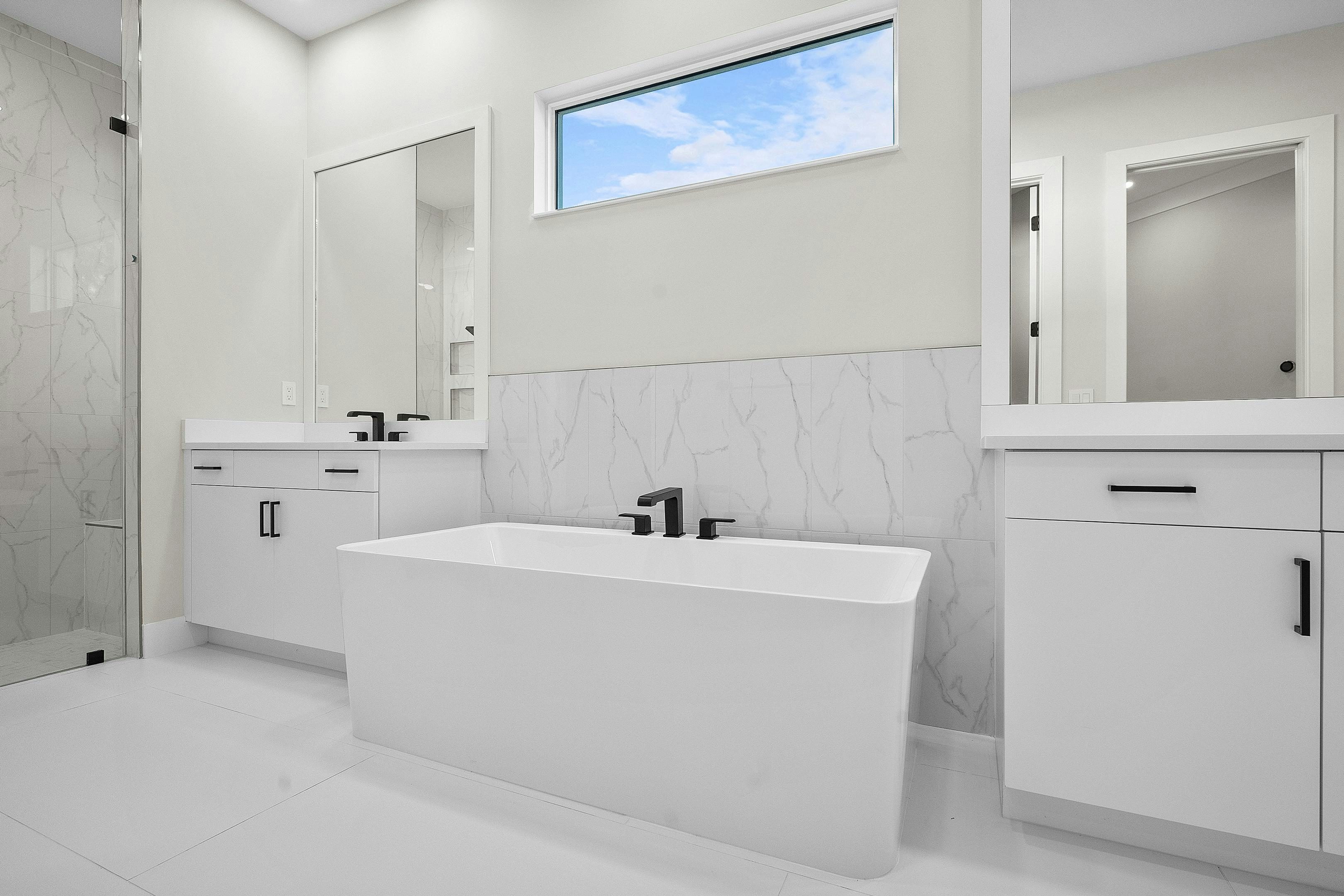 Master bath with modern rectangular soaking tub, split vanity and matte flooring all white