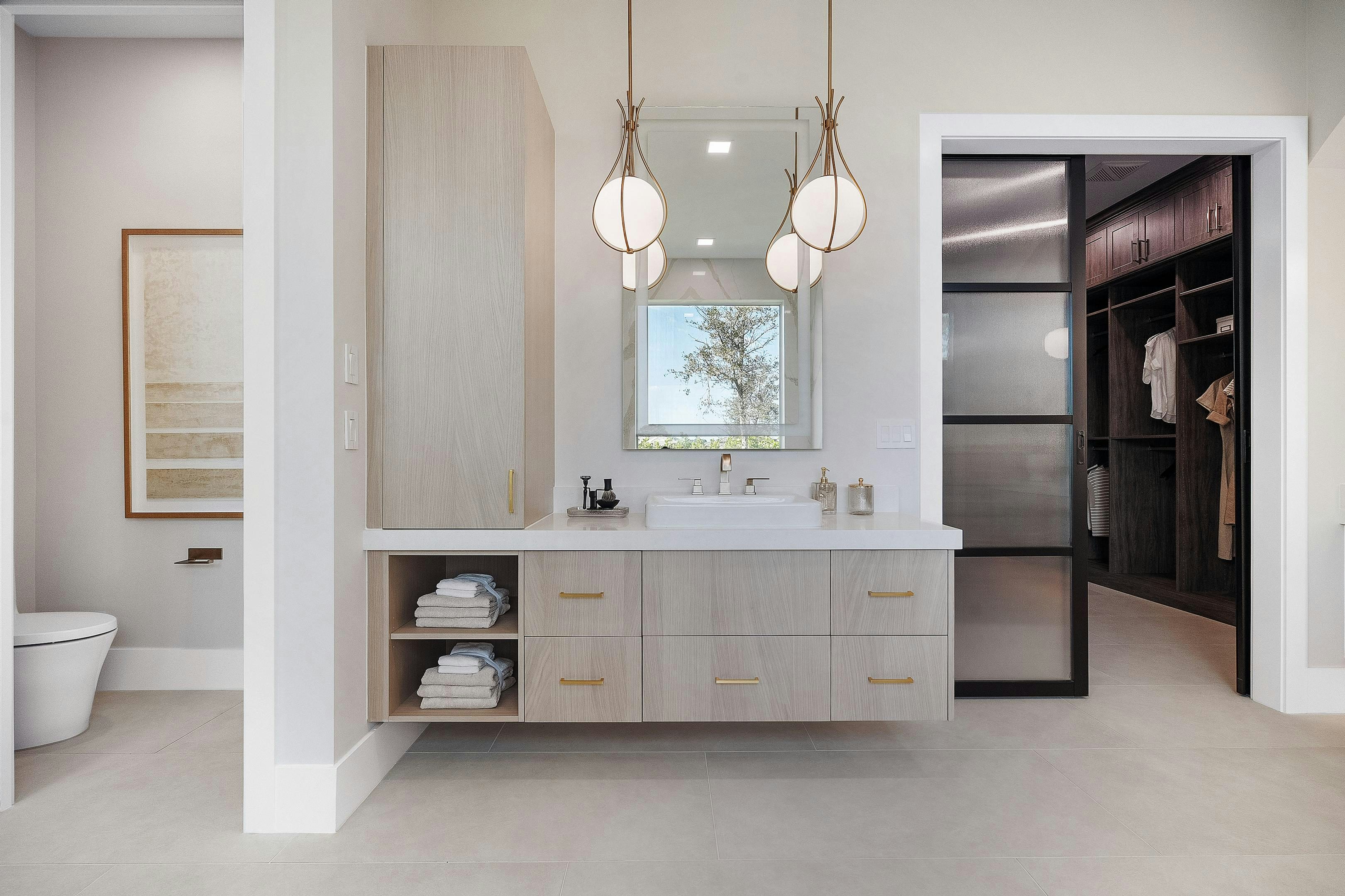 Master bath with floating cabinet with pendant lights and glass door to closet